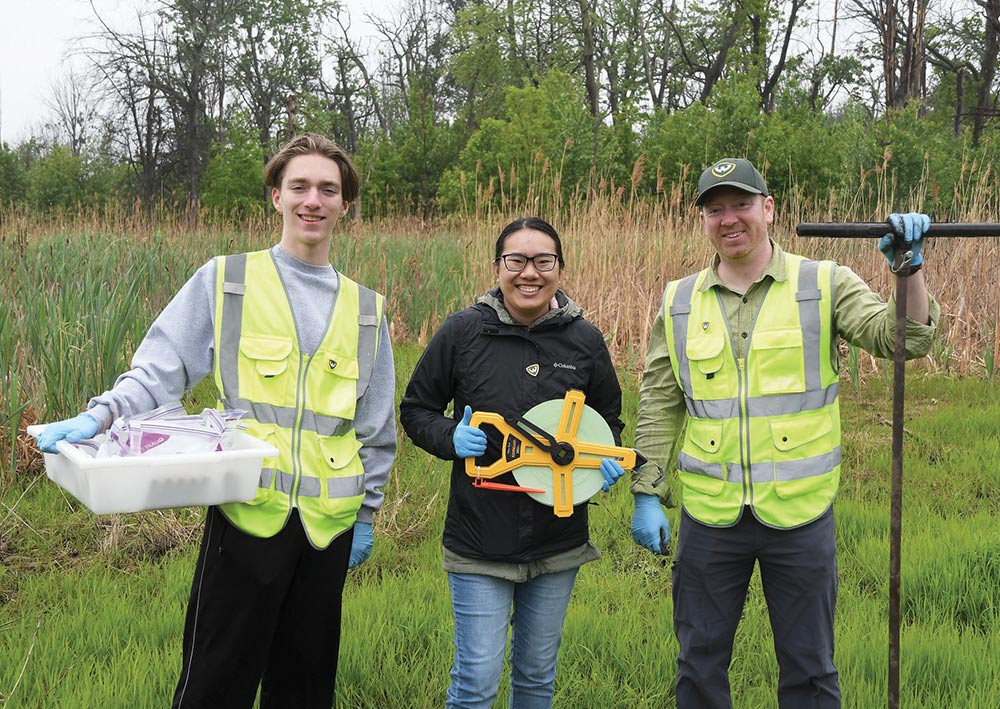 Three students standing in a marshy field